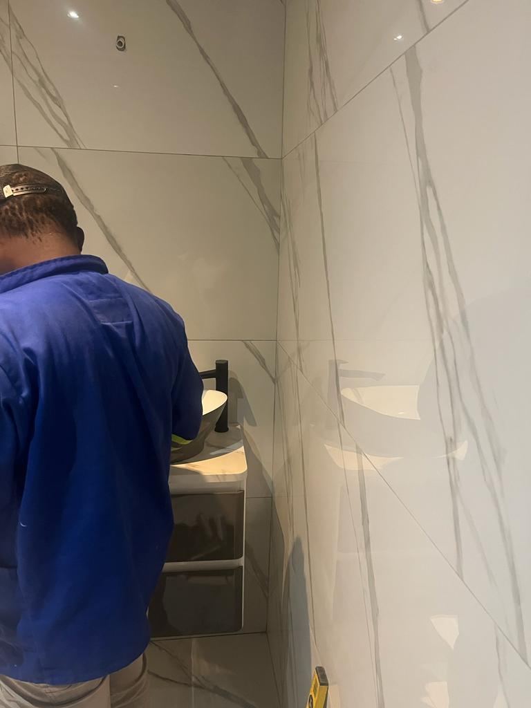 Plumber fitting a basin mixer in a marble-tiled bathroom