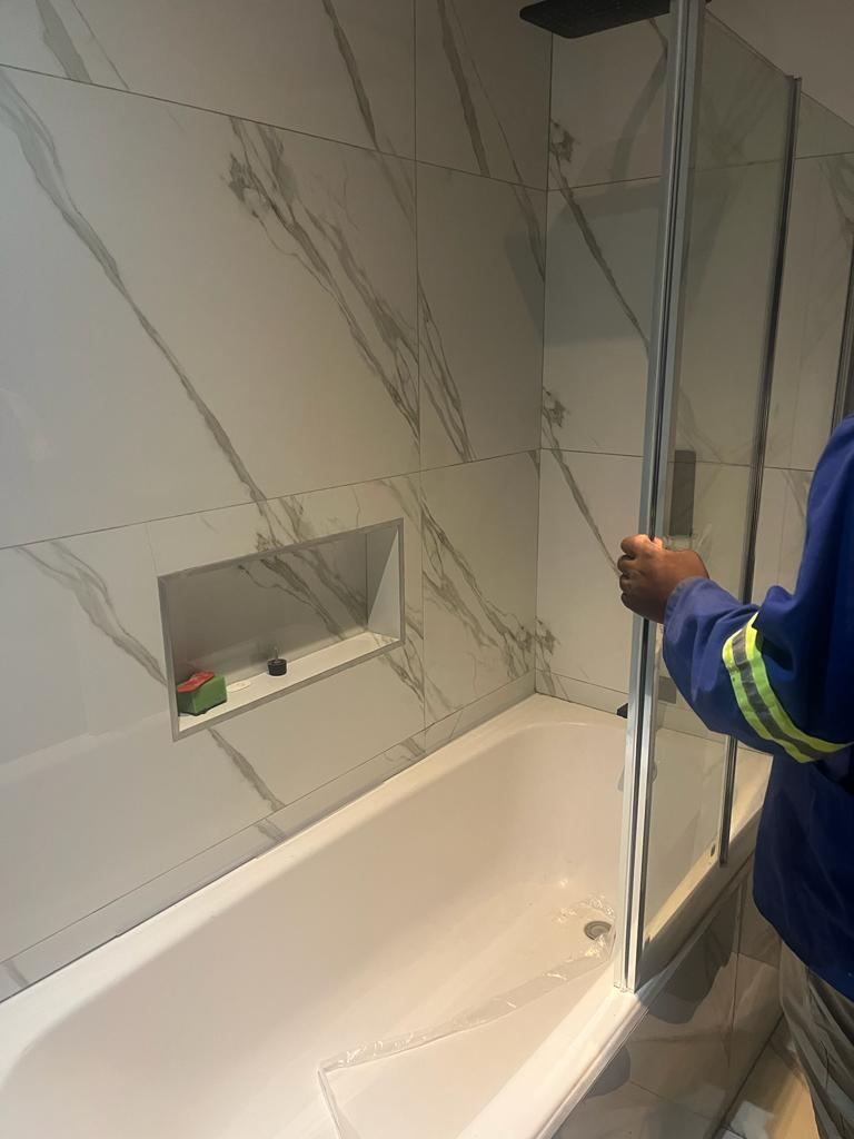 Plumber fitting a glass shower screen to a newly installed bath