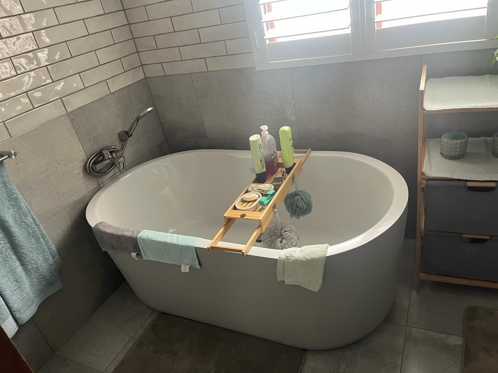 Freestanding bath installed and plumbed in a grey-tiled bathroom