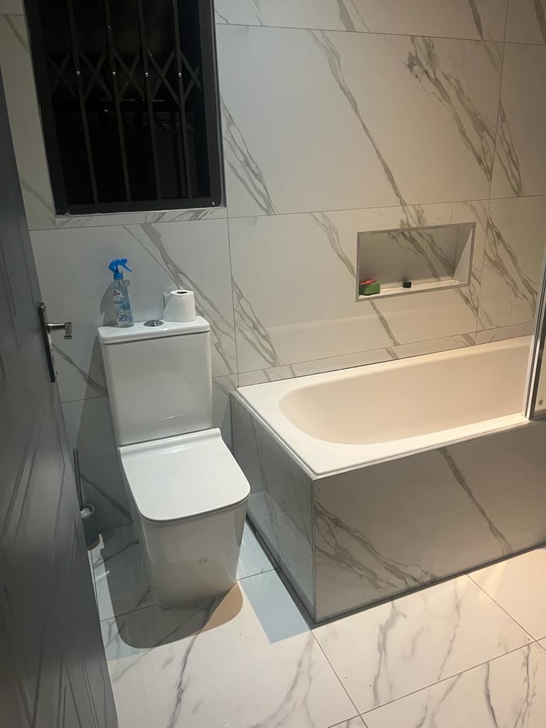 Marble-tiled bathroom with new toilet, bath and recessed shower niche